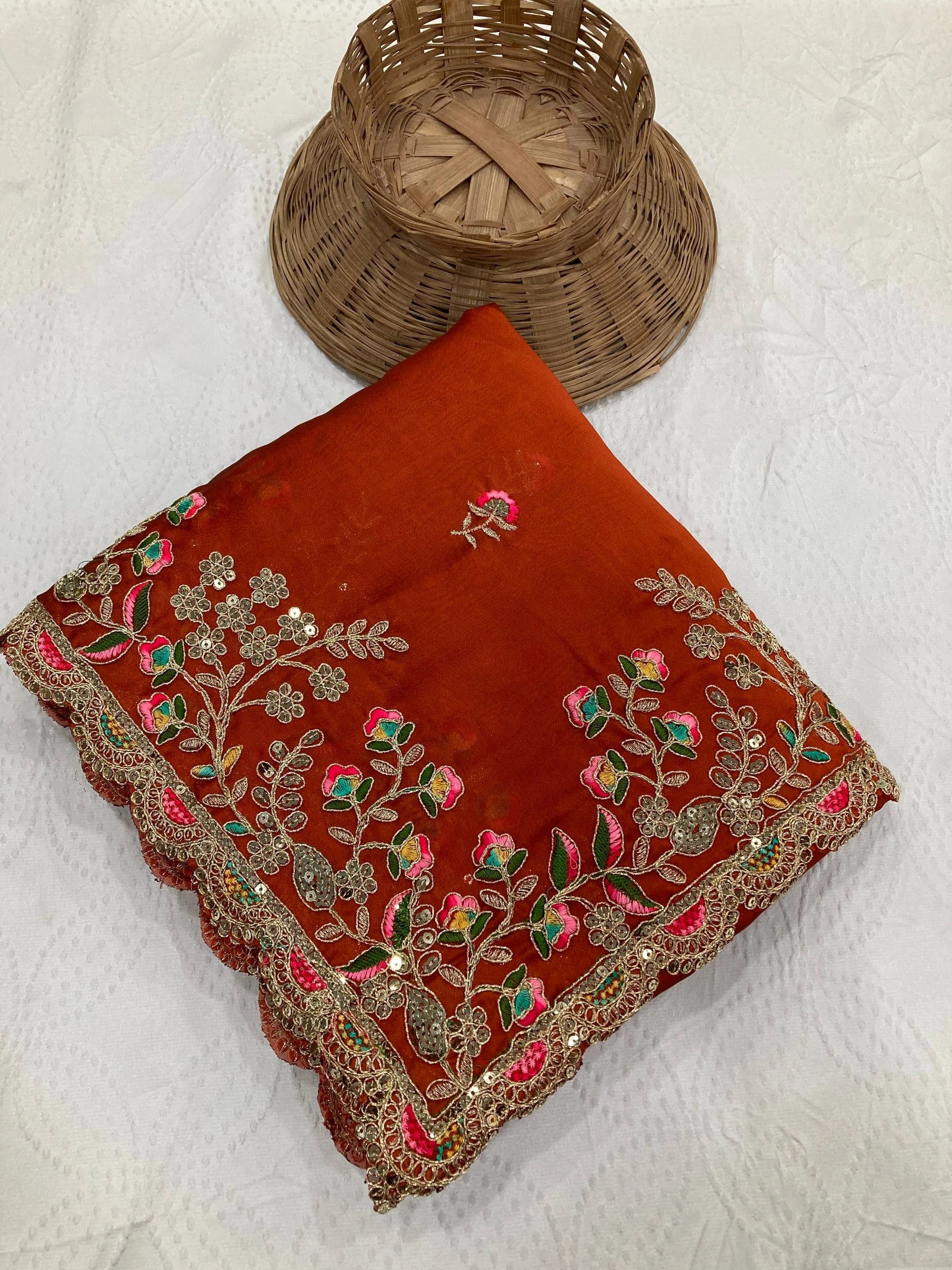 Red embroidered fabric with floral patterns on a textured white surface